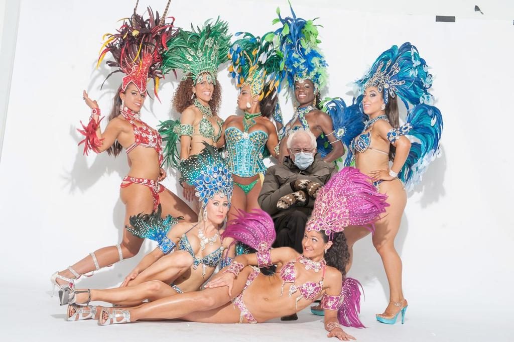 SambaViva dancers in full Carnaval costume with Bernie Sanders sitting in the middle wearing a coat and mittens